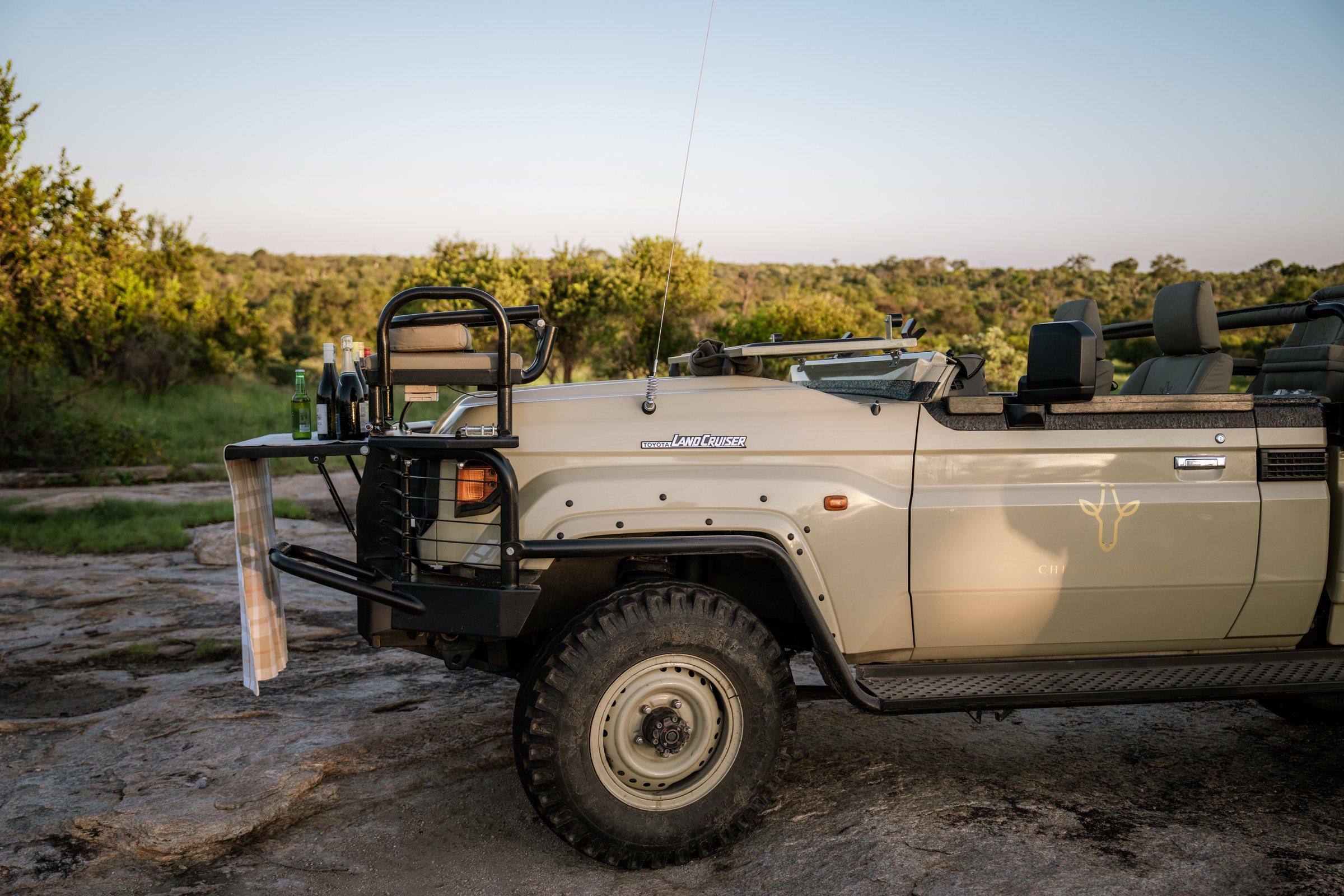 Land Cruiser on a granite outcrop at sundown, drinks set out on the bumper